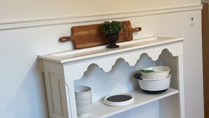 Een witte kast met twee deuren, een klein houten plankje met een plant en een zwarte prullenbak.