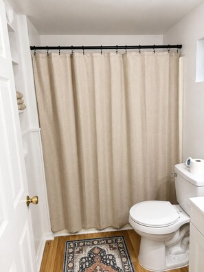 Et badeværelse med et beige brusehæng og toilet samt et mønstret gulvtæppe.