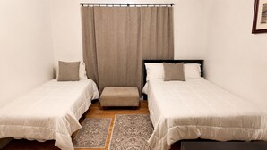 Een slaapkamer met twee eenpersoonsbedden, een bankje, een vloerkleed en een gordijn.