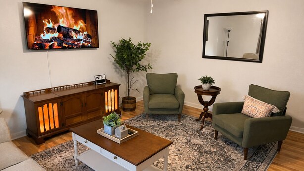 Een woonkamer met een televisie, een bank, een stoel, een kast, een bijzettafeltje en een vloerkleed.