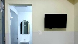 Een kamer met een wit wastafelmeubel, een spiegel, een aan de muur bevestigde televisie, een klein tafeltje en een rode prullenbak.