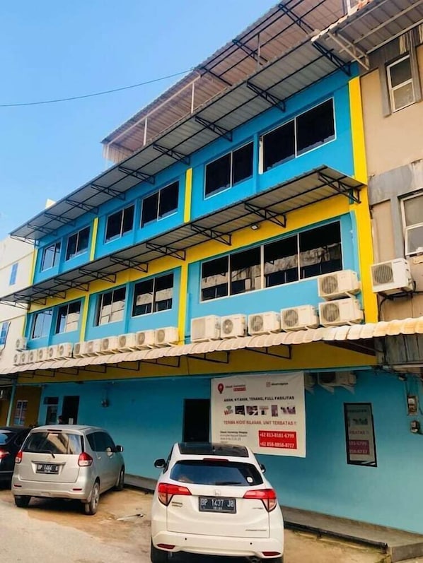Um edifício de vários andares com várias unidades de ar condicionado, uma placa de sinalização e carros estacionados.