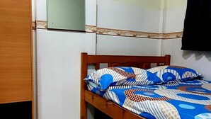 Een kleine kamer met een enkel bed, een houten hoofdbord, een kledingkast van hout en een spiegel aan de muur.