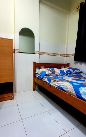 Quarto pequeno com uma cama de solteiro, cabeceira de madeira, guarda-roupa de madeira e um espelho na parede.