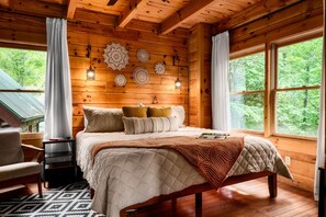 Une chambre dans une cabane en bois, avec un lit, des tables de chevet et une fenêtre donnant sur la forêt.