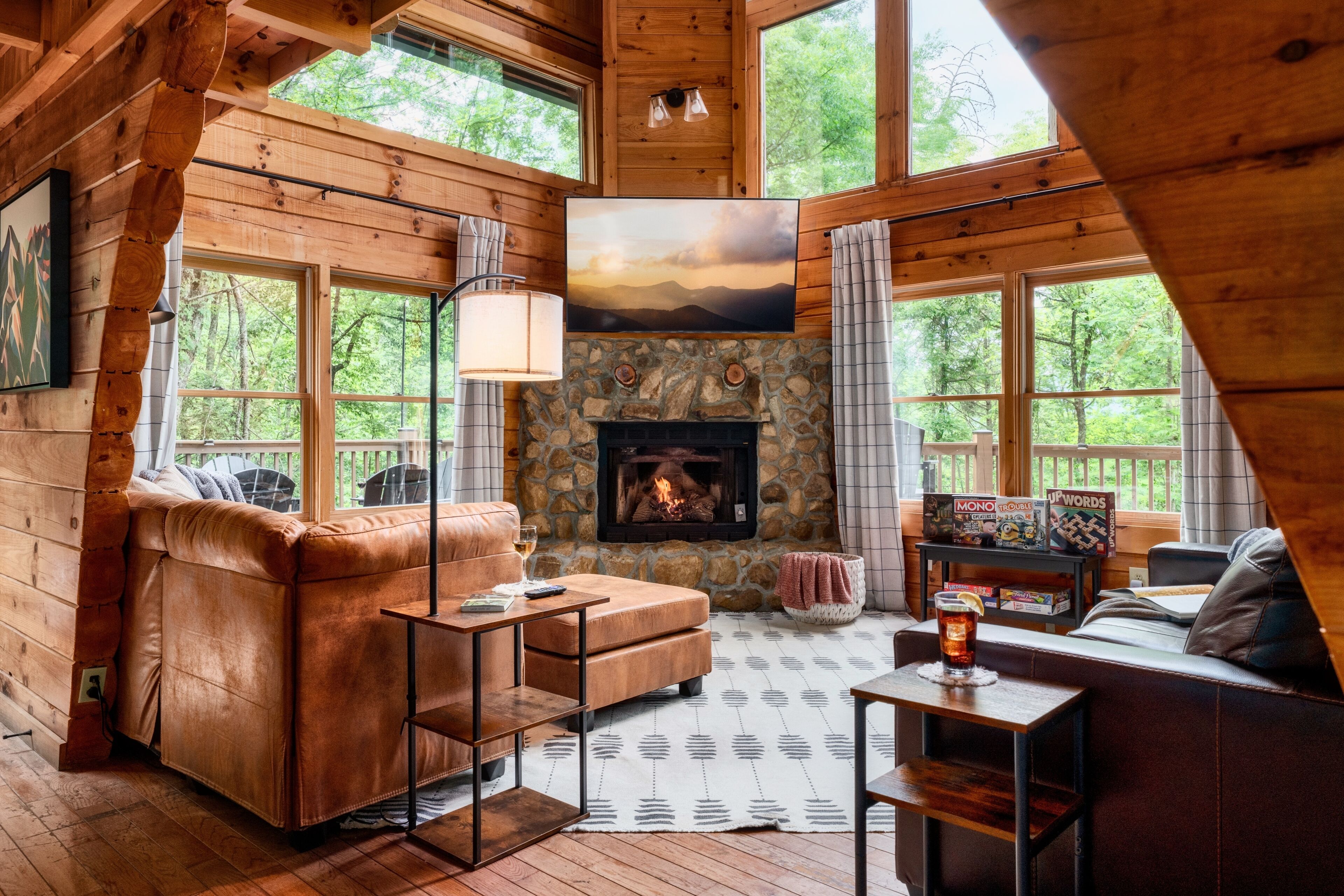 A cozy cabin interior with a stone fireplace, leather sofa, and large windows offering a view of the forest.