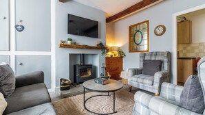 Een gezellige woonkamer met een open haard, een televisie en een geruit fauteuil.