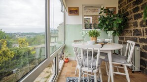 Een balkon met een tafel en stoelen, uitzicht op groen en een bakstenen muur.
