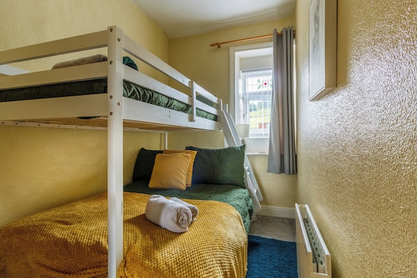 Uma cama beliche com uma toalha enrolada, uma janela com cortinas e um radiador.