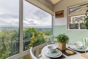 Uma sala de jantar com uma mesa posta para dois, vista para o campo e uma obra de arte emoldurada na parede.
