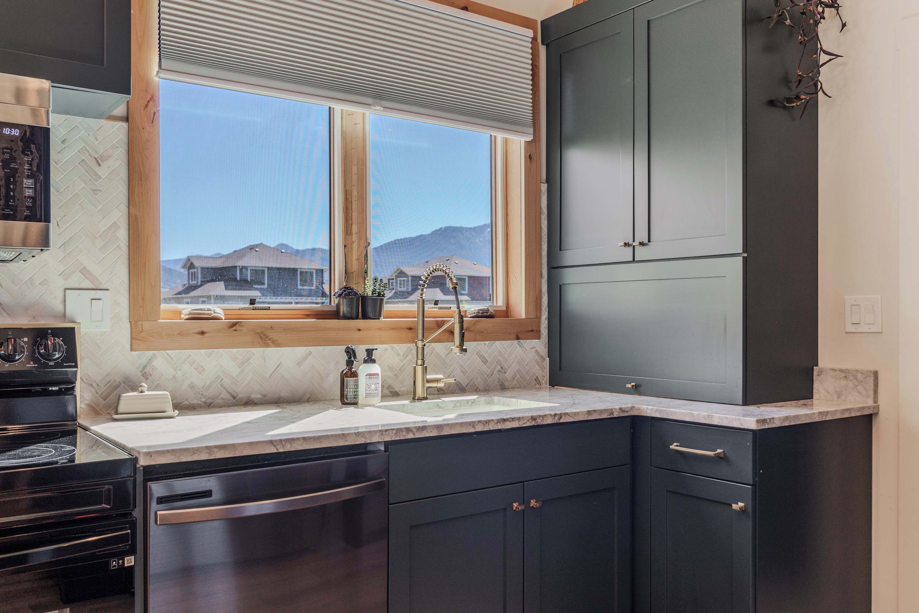 Une cuisine moderne dotée d’une grande fenêtre, d’appareils électroménagers intégrés et de meubles de rangement aux couleurs sombres.