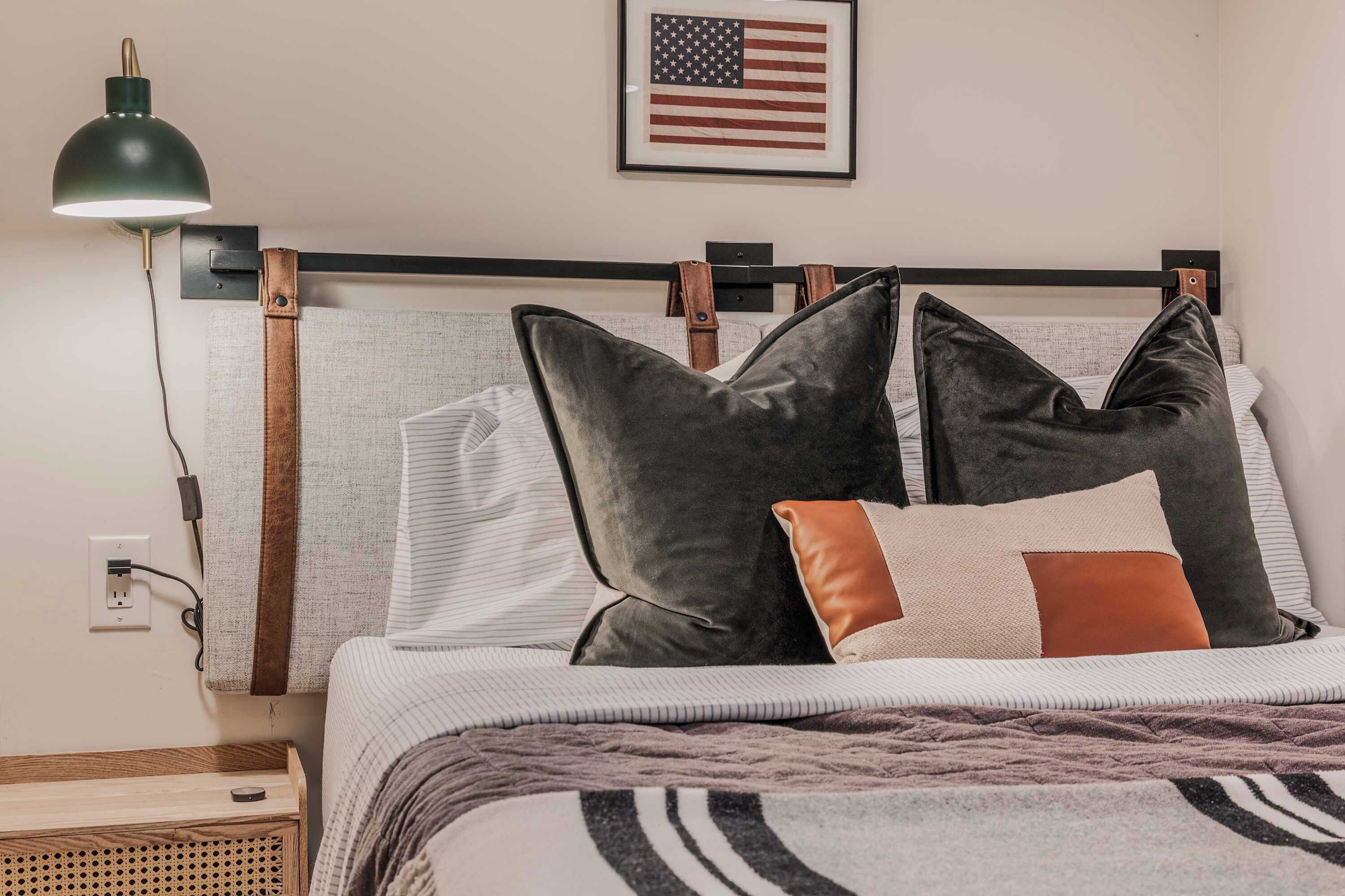 A bed with a headboard, pillows, a blanket, a lamp, and a wall-mounted American flag.