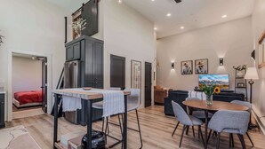 Eine moderne Küche mit integriertem Kühlschrank, ein Essbereich mit rundem Tisch und Stühlen sowie ein Wohnbereich mit Sofa und Fernseher.