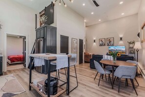 Eine moderne Küche mit integriertem Kühlschrank, ein Essbereich mit rundem Tisch und Stühlen sowie ein Wohnbereich mit Sofa und Fernseher.
