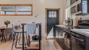 Eine moderne Küche mit Holzboden, eine Essecke mit Stühlen und einem Tisch und eine Aussicht durch ein Fenster.