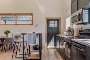 Eine moderne Küche mit Holzboden, eine Essecke mit Stühlen und einem Tisch und eine Aussicht durch ein Fenster.