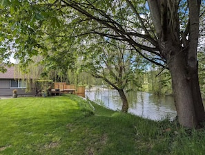 Ein Wohnhaus mit Rasengrundstück, Holzterrasse und einem Gewässer.