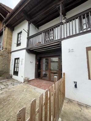 A two-story building with a balcony, a stone wall, and a wooden fence. - Your beach and mountain house in Cantabria. (Casar de Periedo)