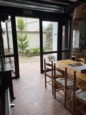 Un espace repas avec une table et des chaises en bois, un panneau indiquant « SORTIE », et une vue sur l’extérieur.