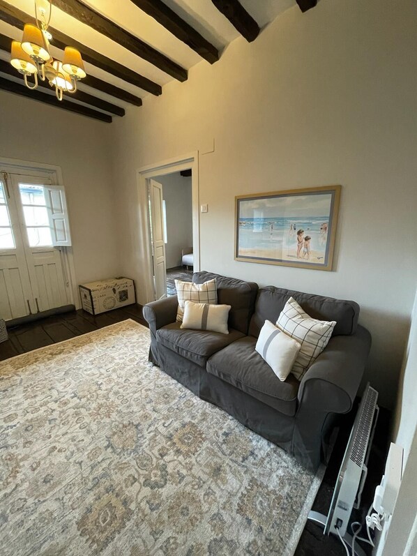 A living room with a dark grey sofa, patterned rug, and a painting of a beach scene. - Your beach and mountain house in Cantabria. (Casar de Periedo)