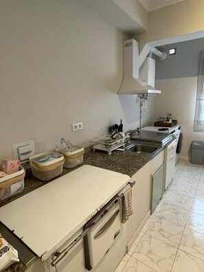Une cuisine avec un plan de travail blanc, un évier, une cuisinière et une fenêtre avec des stores.