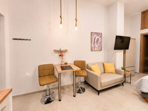 A modern living room with a sofa, two chairs, a small table, and a TV mounted on the wall. - Yellow Rodon • Modern Studio •3 Min Walk to Beach (Chania)