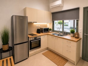 A compact kitchen with a stainless steel refrigerator, a microwave, an oven, a sink, and a window with a view of the street. - Yellow Rodon • Modern Studio •3 Min Walk to Beach (Chania)
