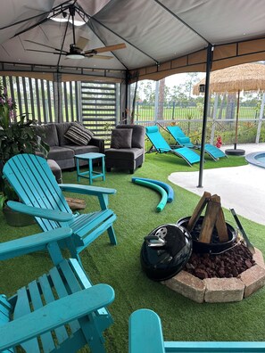 A covered outdoor seating area with a sofa, chairs, and a fire pit.