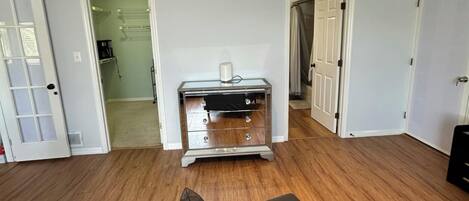 A room with wooden flooring, a mirrored dresser, and a door leading to another room.