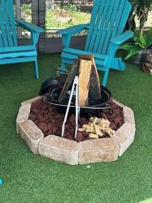 A fire pit with logs, surrounded by a stone border, in a garden with artificial grass and blue chairs. - 1-bedroom bed & breakfast in charming Cape Coral with Pool and laundry service (Cape Coral)