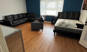 Un dormitorio con sofá, reposapiés, cama y ventana con persianas.