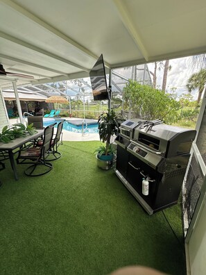 Um pátio coberto com piscina, área de estar externa e churrasqueira.