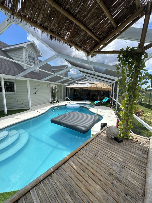 A swimming pool with a floating platform, a covered patio area, and a thatched roof structure.