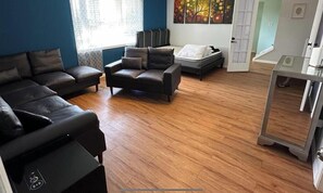 A modern living room with a sectional sofa, a smaller sofa, a bed, and a glass coffee table.