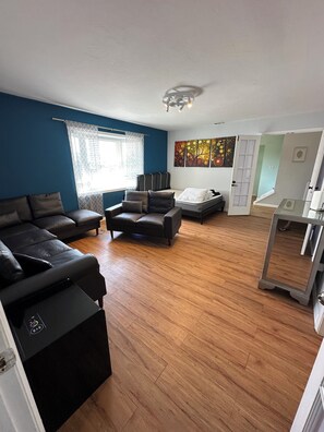 Uma sala de estar com sofá, poltrona, cama e um quadro na parede.
