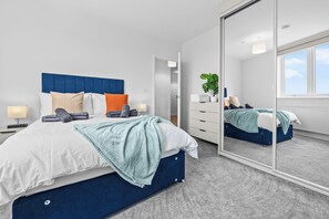 Ein modernes Schlafzimmer mit einem großen Bett, einem Spiegel, einer Kommode und einer Pflanze.