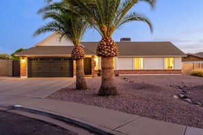 Ein zweigeschossiges Haus mit Garage, zwei Palmen und einem Kiesweg.
