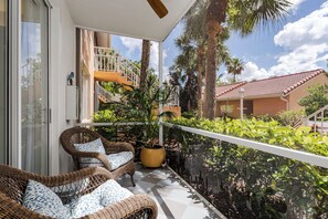 En balkon med fletmøbler, en potteplante og udsigt til en bygning med rødt tag.