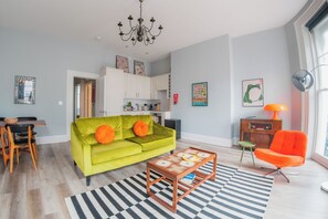 Un salon avec un canapé vert, une table basse en bois, un tapis à rayures et un fauteuil orange vif.