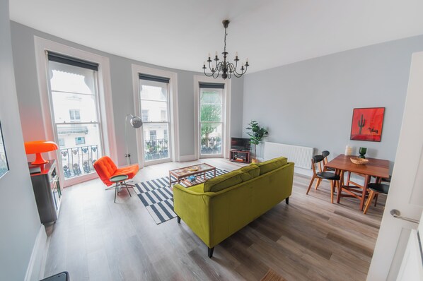 A living room with a sofa, a dining table, and a chandelier. - Sun Soaked Brighton 2 Bed Regency Flat - Sea View (Brighton and Hove)