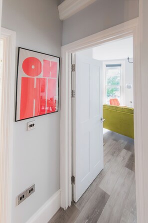 A hallway with a white door leading to a room with a green chair and a window. - Sun Soaked Brighton 2 Bed Regency Flat - Sea View (Brighton and Hove)