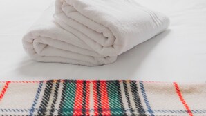 A neatly made bed with white linens and pillows, a folded towel on the bed, and a window with a view of buildings. - Sun Soaked Brighton 2 Bed Regency Flat - Sea View (Brighton and Hove)