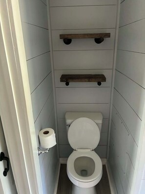 Un baño pequeño y estrecho con un inodoro, estantes de madera y un rollo de papel higiénico.