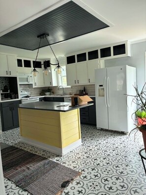 Una cocina moderna con armarios blancos, una isla central y un suelo estampado.