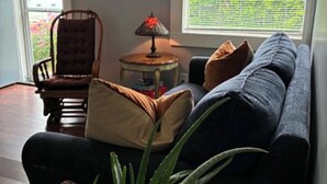 A living room with a sofa, a chair, a lamp, a plant, and a window with blinds.