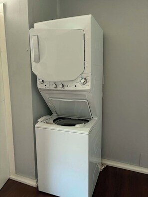 A compact, white front-loading washing machine with a control panel, placed against a plain wall. - The City Acre- A cozy lil private farmhouse 12 min from Fort Worth and Arlington (Fort Worth)
