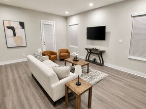 Ein Wohnzimmer mit einer Couch, zwei Sesseln, einem Couchtisch, einem Fernseher und einem Kamin.