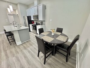 A modern kitchen with white cabinets, a central island, and a dining area with a round table and black chairs.