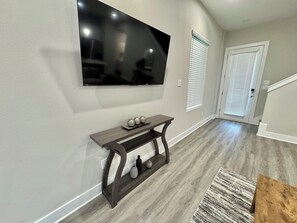 A modern living room with a flat-screen TV mounted on the wall, a wooden console table with decorative items, and a patterned rug on the floor.