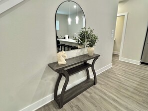 A hallway with a dark wooden console table, a white horse sculpture, a potted plant, and a large mirror reflecting a dining area.